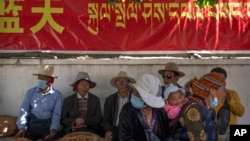 FILE - People rest in the shade beneath a government propaganda banner in Chinese and Tibetan near a neighborhood Tibetan Buddhist shrine in Lhasa, the capital of China's Tibet Autonomous Region, on June 3, 2021.