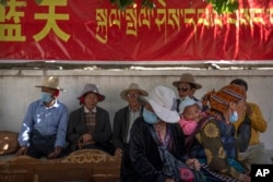 FILE - People rest in the shade beneath a government propaganda banner in Chinese and Tibetan near a neighborhood Tibetan Buddhist shrine in the Chengguan district of Lhasa in western China's Tibet Autonomous Region, June 3, 2021. (AP Photo/Mark Schiefelbein, File)