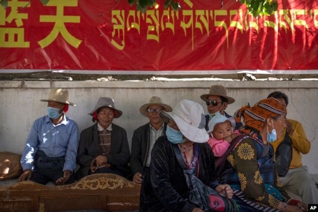 FILE - People rest in the shade beneath a government propaganda banner in Chinese and Tibetan near a neighborhood Tibetan Buddhist shrine in the Chengguan district of Lhasa in western China's Tibet Autonomous Region, June 3, 2021. (AP Photo/Mark Schiefelbein, File)