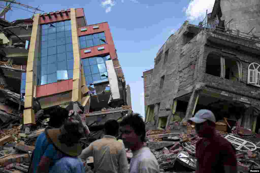 Orang-orang berjalan melewati sebuah gedung yang runtuh akibat gempa berkekuatan 7,3 skala Richter yang mengguncang Kathmandu, Nepal.