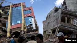 FILE - People walk past a collapsed building after a 7.3 earthquake struck, in Kathmandu, Nepal, May 12, 2015.