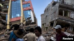 People walk past a collapsed building after a fresh 7.3 earthquake struck, in Kathmandu, Nepal, May 12, 2015.