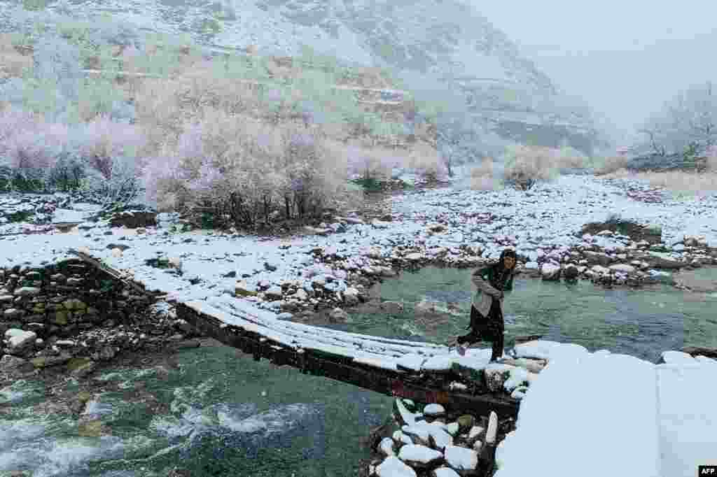 An Afghan boy walks across a footbridge during the first snowfall in the Dara district of Afghanistan&#39;s Panjshir province.