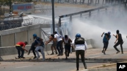 Anti-government protesters are sprayed with a water canon by security forces behind the perimeter wall of La Carlota airbase in Caracas, Venezuela, May 1, 2019.