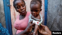 Cherlande Dolcine, 20, holds her daughter Dainaika Jean, 2, in front of their house as a measurement shows red for severe malnourishment in Port-de-Paix, Haiti, Jan. 30, 2020. 