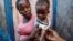 Cherlande Dolcine, 20, holds her daughter Dainaika Jean, 2, in front of their house as a measurement shows red for severe malnourishment in Port-de-Paix, Haiti, Jan. 30, 2020. 