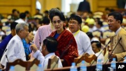 FILE - NLD leader Aung San Suu Kyi, covered in a red scarf, stands among the lawmakers of her party ahead of a regular session of Myanmar's lower house of parliament in Naypyidaw, Jan. 7, 2016.