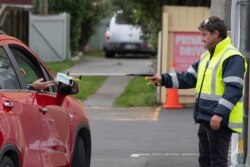 A security guard, right, hands a face mask to a visitor in a car by using a stick outside a COVID-19 coronavirus clinic in Lower Hutt, near Wellington, April 20, 2020.