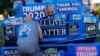 A supporter of U.S. President Donald Trump ties off a banner hanging from a boom during Super Happy Fun America&#39;s &quot;Back the Blue/President Trump Standout&quot; in Stoneham, Massachusetts, July 27, 2020.