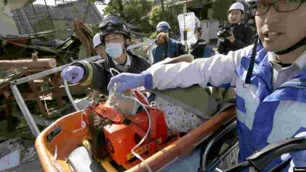 A woman is carried away by rescue workers after being rescued from her collapsed home caused by an earthquake in Mashiki town, Kumamoto prefecture, southern Japan, in this photo taken by Kyodo, April 16, 2016.