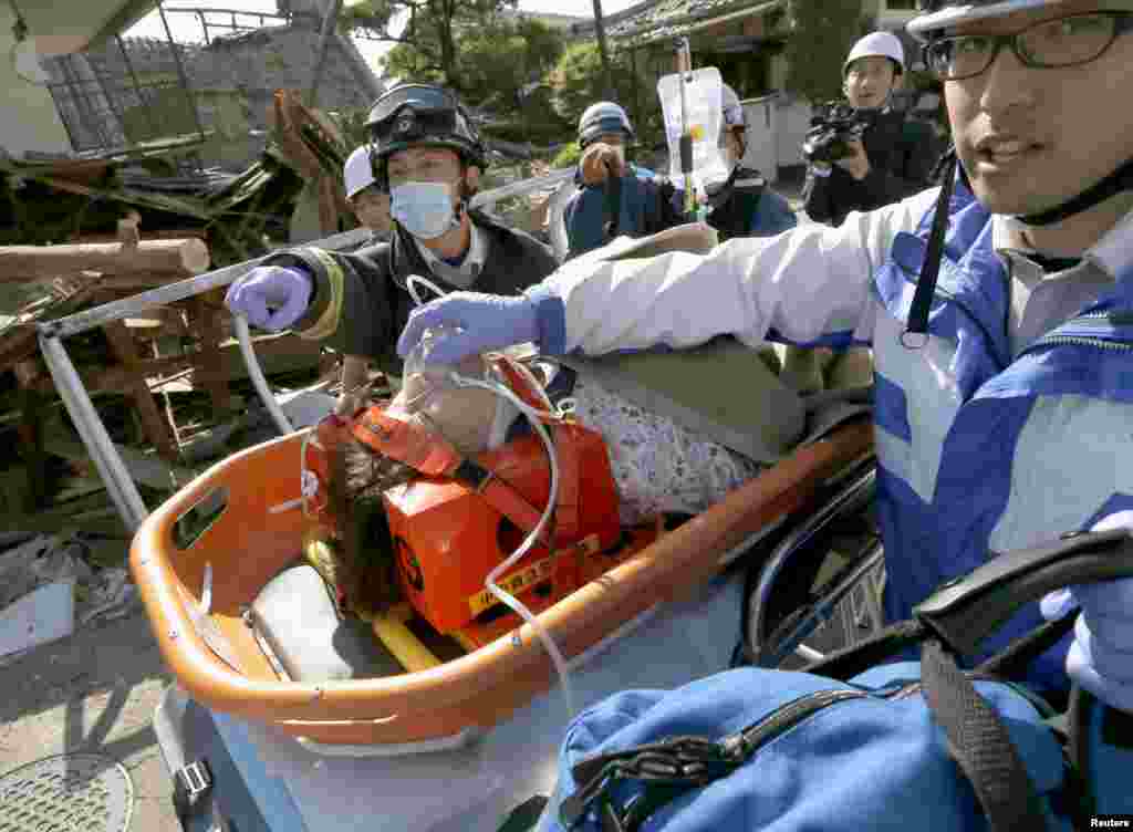 A woman is carried away by rescue workers after being rescued from her collapsed home caused by an earthquake in Mashiki town, Kumamoto prefecture, southern Japan, in this photo taken by Kyodo, April 16, 2016.
