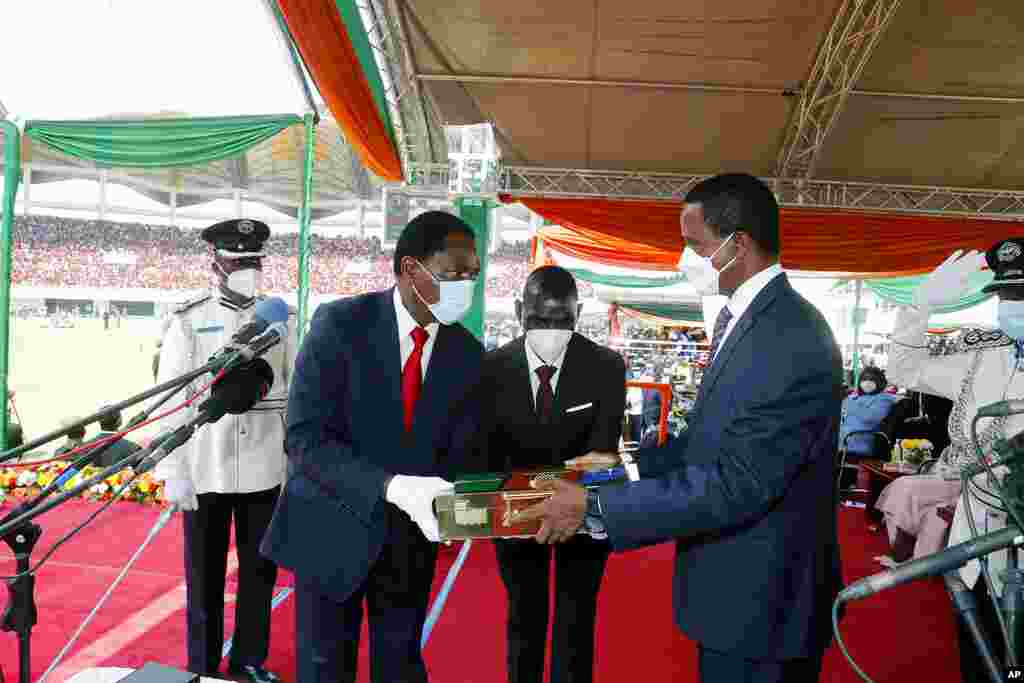 O Presidente cessante da Zâmbia, Edgar Chagwa Lungu, à direita, entrega os instrumentos do poder ao seu sucessor, o Presidente Hakainde Hichilema, durante a cerimónia de inauguração no Estádio Heróis em Lusaka, Zâmbia, terça-feira, 24 de Agosto de 2021.