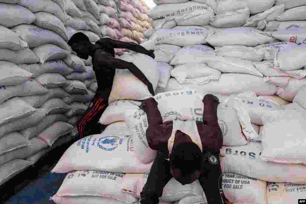 Sudanese local community members carry to deliver sacks of sorghum for Ethiopian refugees who fled the country&#39;s Tigray conflict, in a warehouse erected by the World Food Program (WFP) at Um Raquba refugee camp in Gedaref, eastern Sudan.