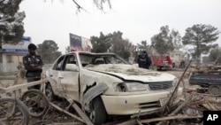 Afghan policemen inspect a car hit by a suicide car bomb attack in Khost province, February 18, 2011