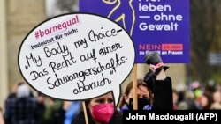 Seorang pengunjuk rasa mengangkat papan bertuliskan "Tubuhku pilihanku - hak untuk aborsi" selama demonstrasi menentang kekerasan terhadap perempuan yang disebut oleh organisasi hak perempuan "Terre des Femmes" di depan Gerbang Brandenburg di Berlin, pada