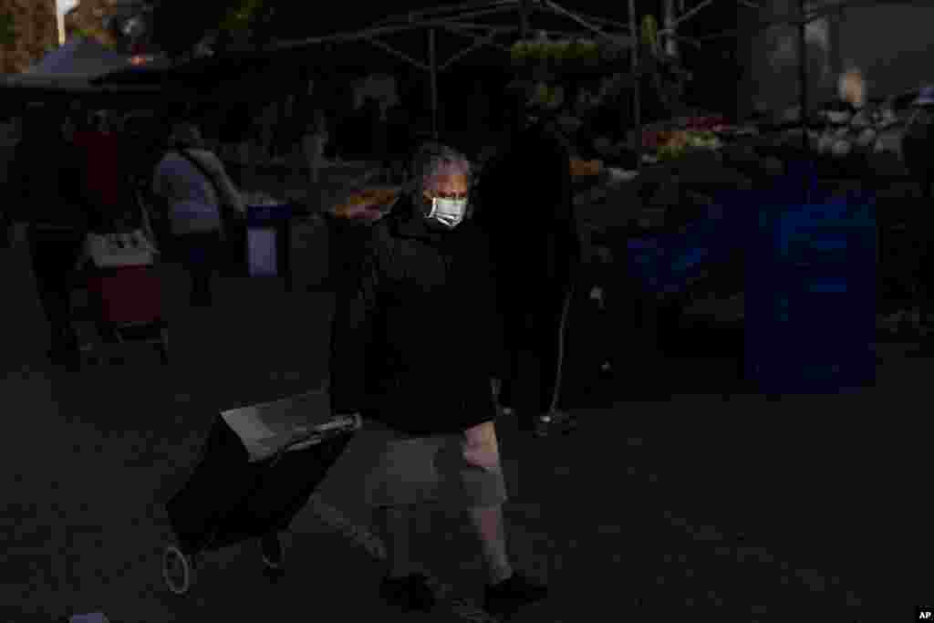 An elderly woman wearing a face mask to prevent the spread of coronavirus walks along street stalls at a fruit market in Madrid, Spain, Tuesday, Oct. 13, 2020. (AP Photo/Bernat Armangue)