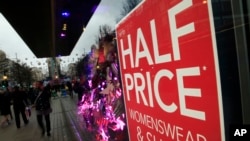 Christmas shoppers walk past a sale sign in the window of a shop in Oxford Street in London, Friday, Dec. 18, 2015. 