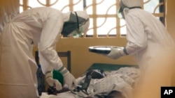 In this 2014 photo provided by the Samaritan's Purse aid organization, Dr. Kent Brantly, left, treats an Ebola patient at the Samaritan's Purse Ebola Case Management Center in Monrovia, Liberia.