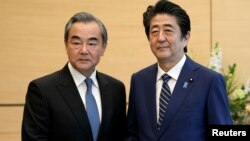 中国外长王毅在东京与日本首相安倍晋三握手。（2019年11月25日）