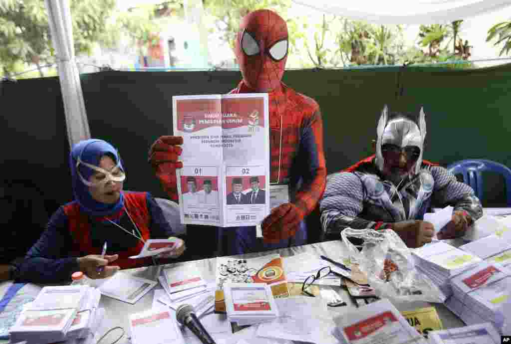 Para petugas KPPS mengenakan kostum superhero menunjukkan kertas suara untuk pemilihan presiden di sebuah TPS di Surabaya, 17 April 2019. (Foto: Trisnadi/AP) 