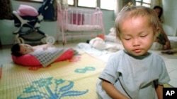 A young orphaned Cambodian infant girl infected with the HIV virus sits on a mat in the Phnom Penh Nutrition Center.