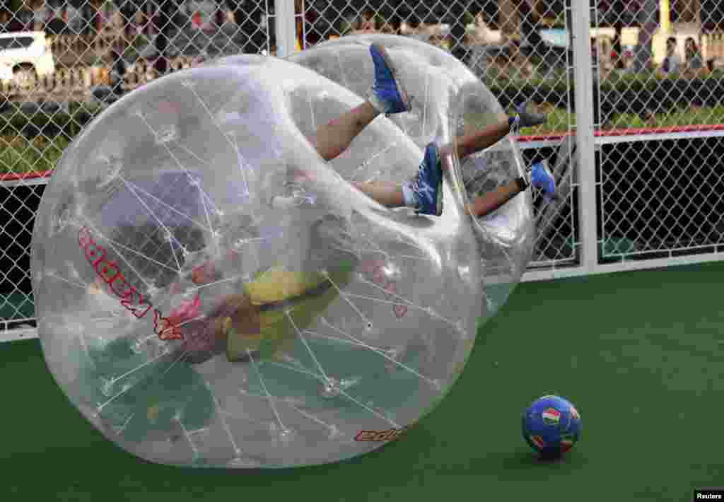Players partially encased in giant plastic inflatable balls roll over on the ground, their legs in the air, during their bubble soccer match in Beijing, China.