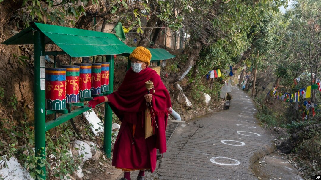 Seorang biksu Buddha Tibet di pengasingan memutar roda doa di jalan yang ditandai dengan lingkaran bagi para pemilih yang antre untuk memberikan suara, guna memastikan jarak sosial, selama pemilu di Dharamsala, India, Minggu (3/1). 