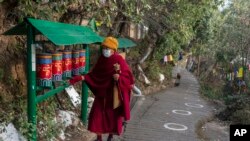 Seorang biksu Buddha Tibet di pengasingan memutar roda doa di jalan yang ditandai dengan lingkaran bagi para pemilih yang antre untuk memberikan suara, guna memastikan jarak sosial, selama pemilu di Dharamsala, India, Minggu (3/1). 