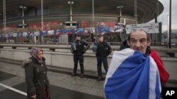 A French supporter wrapped in his national flag passes by police officers guarding the Stade de France stadium prior to the international exhibition soccer match between France and Russia in Saint Denis, north of Paris, March 29, 2016.