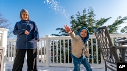 Omar Abu Kuwaik throws snow shortly after arriving from Gaza at the residence of the Global Medical Relief Fund as Khaolah Obahi of Rahma Worldwide looks on, Wednesday, Jan. 17, 2024. (AP Photo/Peter K. Afriyie)