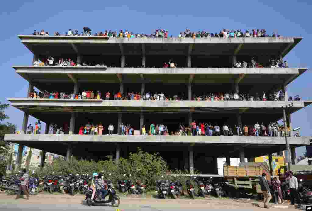 People stand on an under construction building outside Yelahanka air base and watch Indian Air Force Suryakiran aircrafts perform aerobatic maneuvers on the second day of Aero India 2021 in Bengaluru, India.