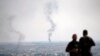 FILE - TV journalists work from a hilltop in southeastern Turkey, as in the background smoke billows from a fire in Ras al-Ayn, Syria, Oct. 20, 2019. 