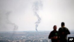 FILE - TV journalists work from a hilltop in southeastern Turkey, as in the background smoke billows from a fire in Ras al-Ayn, Syria, Oct. 20, 2019. 