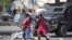 Pedestrians run past an armored police car in Port-au-Prince, Haiti, on March 7, 2024. Unrelenting gang attacks in Haiti have paralyzed the country and left it with dwindling supplies of basic goods.
