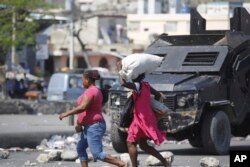 Pejalan kaki melewati mobil polisi lapis baja di Port-au-Prince, Haiti, Kamis, 7 Maret 2024. (Foto: AP)