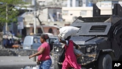 FILE - Pedestrians run past an armored police car in Port-au-Prince, Haiti, March 7, 2024.