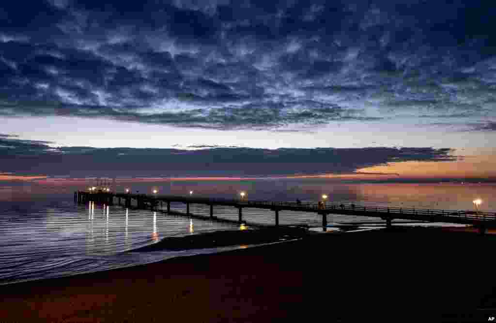 Lamps shine on a pier during sunrise at the Baltic Sea in Scharbeutz, northern Germany, Tuesday, Oct. 13, 2020. (AP Photo/Michael Probst)