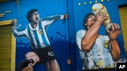 Augusto Canosa prays while touching a painting of Diego Maradona near the Boca Juniors stadium in Buenos Aires, Argentina, Nov. 27, 2020. The Argentine soccer great died from a heart attack at his home Nov. 25 at age 60.
