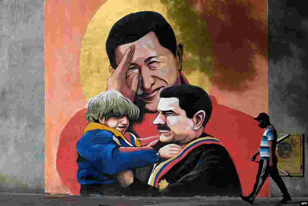 A man walks past a mural depicting Venezuelan late President Hugo Chavez, center, saluting and Venezuelan President Nicolas Maduro, right, holding a child in Caracas.
