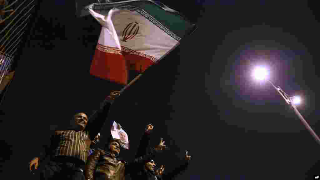 Iranianos abanam a bandeira nacional e envergam um cartaz do Presidente Hassan Rouhani, para dar as boas-vindas aos negociadores nucleares que chegavam de Geneva. Teerão, Nov. 24, 2013.