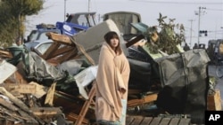 A Japanese woman draped in a blanket stands in the rubble from Friday's quake and tsunami, Sunday, March 13, 2011.