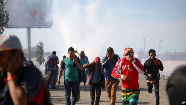 Migrantes se cubren la cara, mientas huyen de gas lacrimógeno, lanzado por la patrulla fronteriza de Estados Unidos, cerca a la valla entre EE.UU. y México en Tijuana, México, el 25 de noviembre del 2018