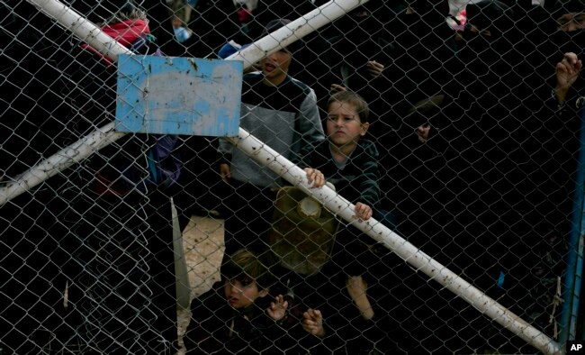 FILE - Children peer from the gate that closes off the section for foreign families who live in the Islamic State group's so-called caliphate, at al-Hol camp in Hassakeh province, Syria, March 31, 2019.