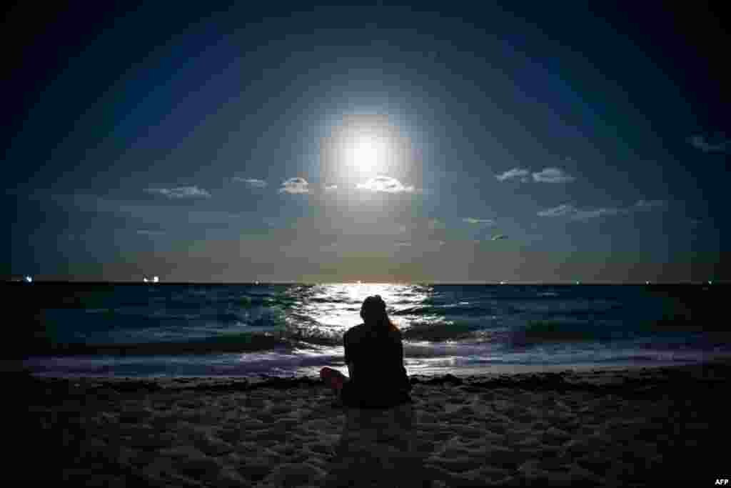 A Super Pink Full Moon lights up the sky as a person relaxes on the beach in Miami Beach, Florida, April 26, 2021.