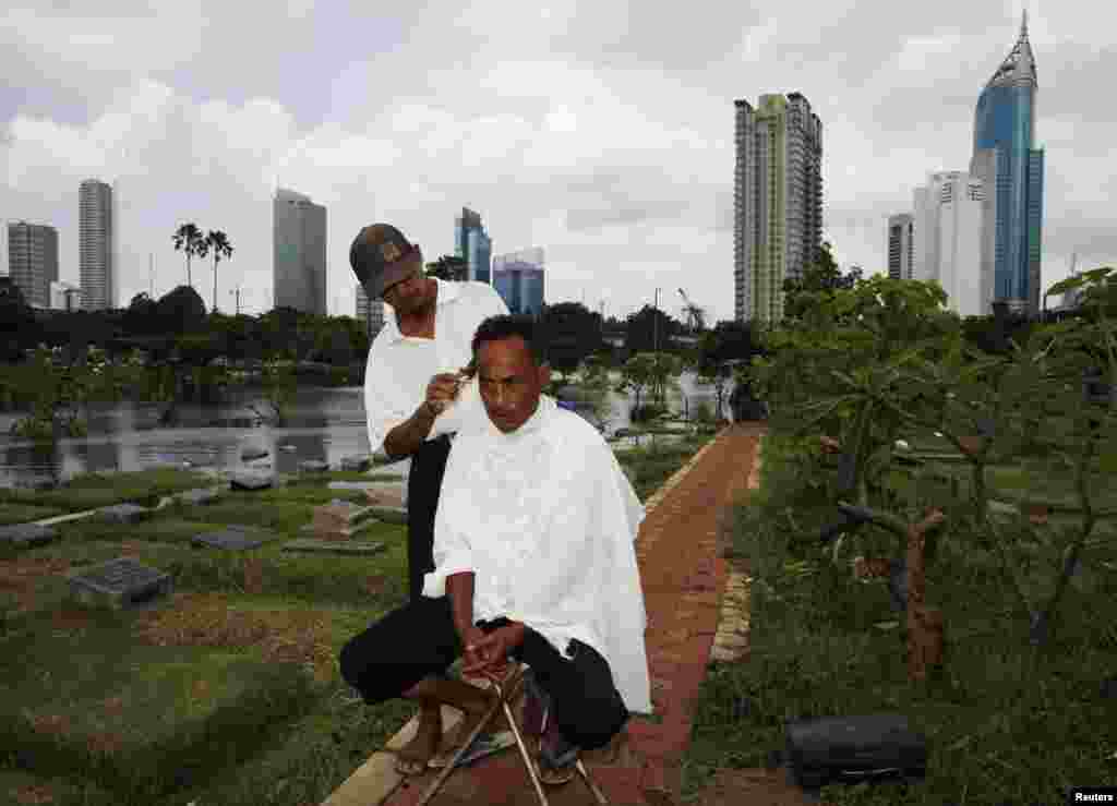 Cemetery worker Mohammad Udin has his hair cut by a mobile barber as the flooded cemetery complex is pictured in the background in Jakarta, Indonesia.