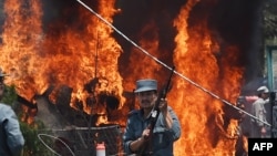 An Afghan policeman stands guard as smoke and flames rise from the site of a huge blast struck near the entrance of Kabul's international airport, in Kabul on August 10, 2015. 