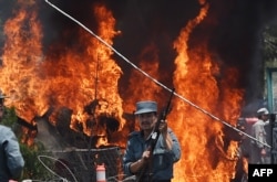 FILE - An Afghan policeman stands guard as smoke and flames rise from the site of a huge blast struck near the entrance of Kabul's international airport, in Kabul on August 10, 2015.