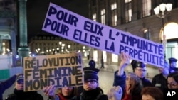 FILE - A feminist activist holds placards near the Justice Ministry during a protest calling to change French statutory rape laws after a man was acquitted of raping an 11-year-old, in Paris, Nov. 14, 2017. 