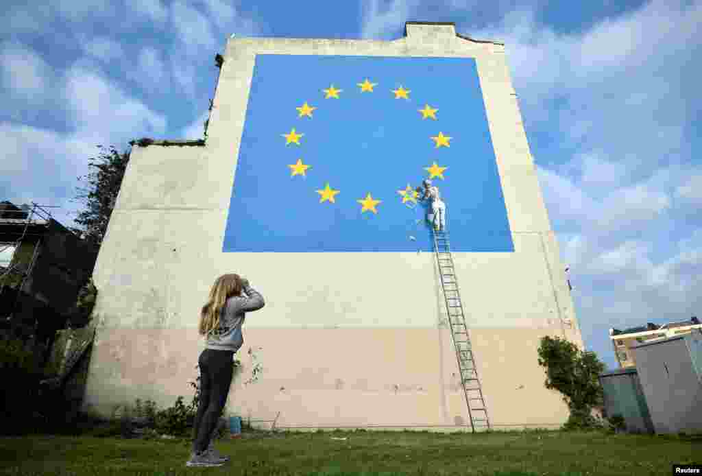 A young girl looks at an artwork attributed to street artist Banksy, depicting a workman chipping away at one of the 12 stars on the European Union, on a wall in the ferry port of Dover, Britain, May 7, 2017.