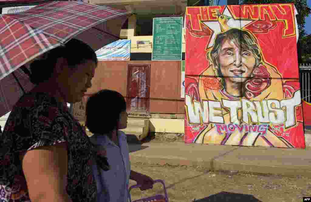 Orang-orang berjalan melewati graffiti pemimpin oposisi Myanmar Aung San Suu Kyi di luar kantor pusat Partai Liga Nasional untuk Demokrasi (NLD) di Yangon. Partai Aung San Suu Kyi memenangkan mayoritas bangku parlemen sebagai hasil dari pemilu minggu lalu yang memungkinkan partai tersebut memilih presiden dan membentuk pemerintahan dalam sebuah pergeseran kekuasaan bersejarah dari militer.